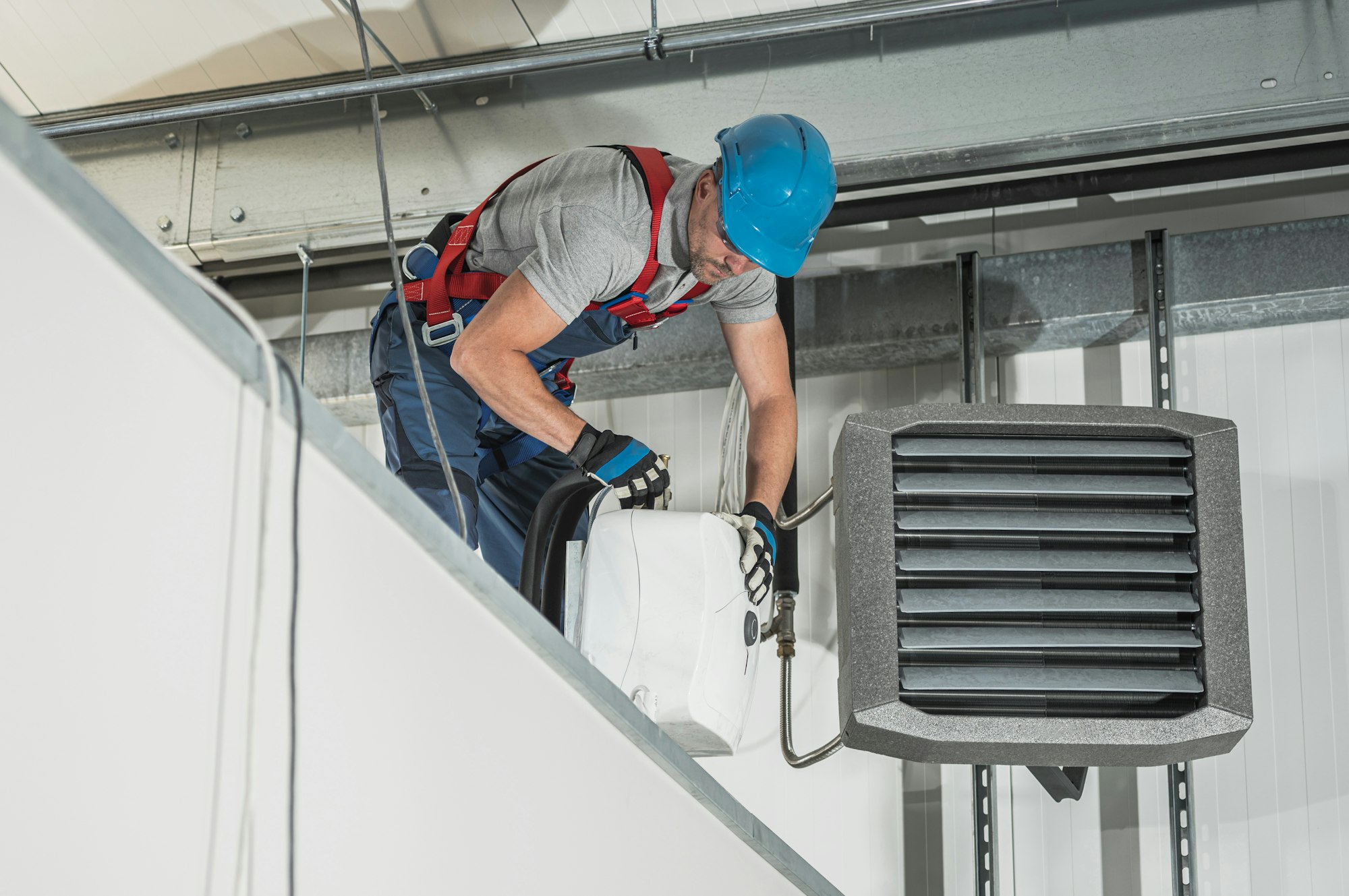 HVAC Technician Installing New Warehouse Air and Water Heaters, Technician in a hard hat installing a wall-mounted unit heater to boost heating in Springdale - AR