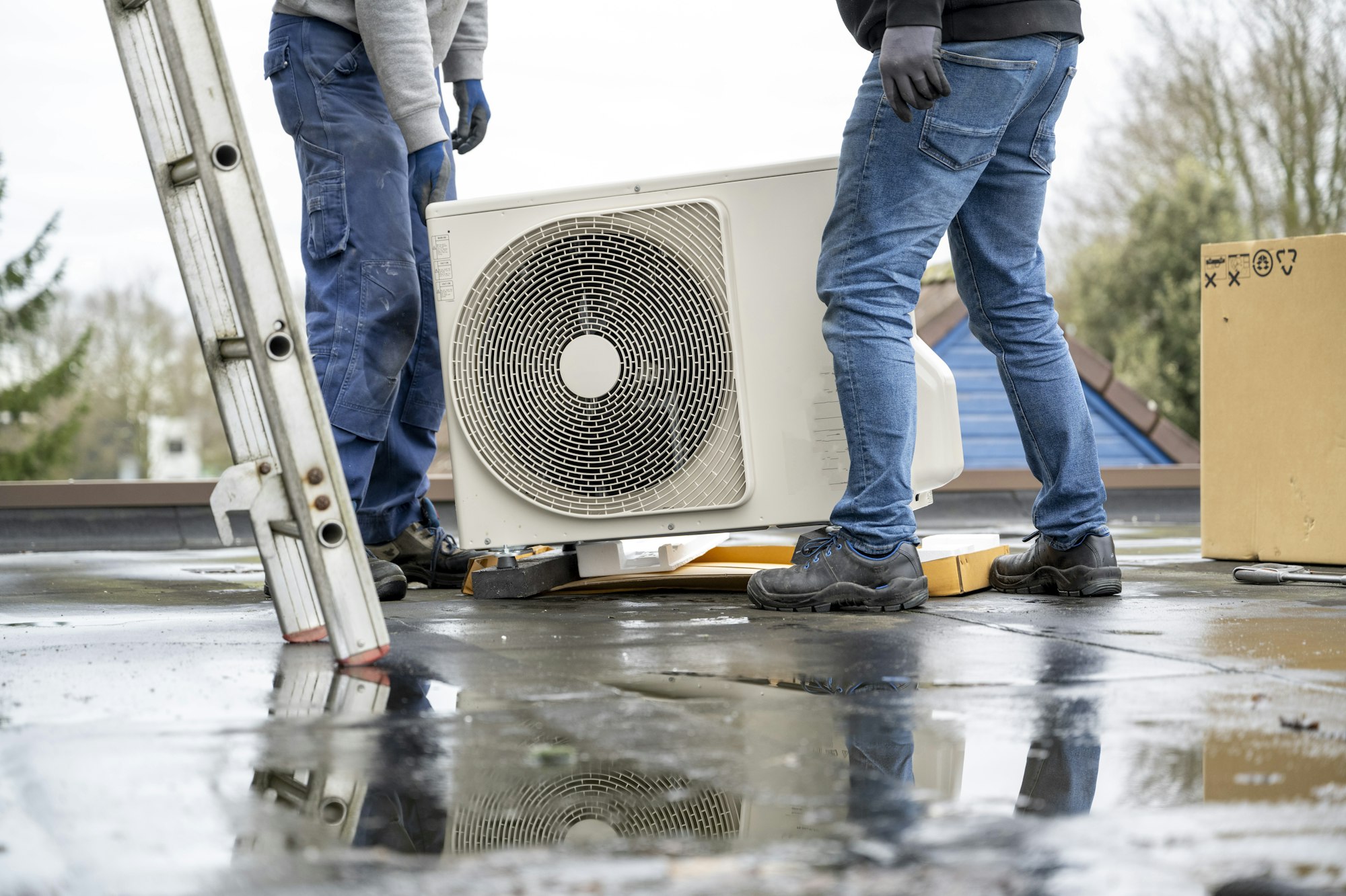 Two workers installing an air conditioning unit on a rooftop on a cloudy day.